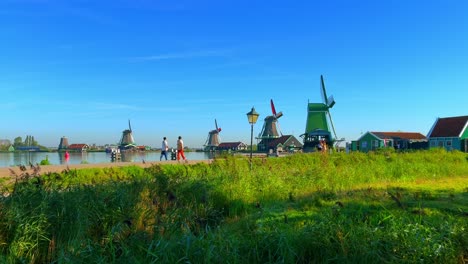 People-pass-by-the-Traditional-Dutch-windmills-and-houses-near-the-canal-in-Zaanse-Schans,-Netherlands,-Europe