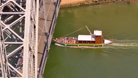 Barco-Con-Turistas-Pasando-Cerca-Del-Puente-Dom-Luís-I-En-Oporto,-Portugal.