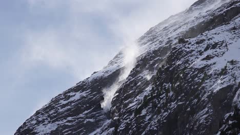 Close-up-of-podary-snow-getting-blown-around-on-a-mountain-cliff-ridge-on-a-snowy-rocky-glacier-slope