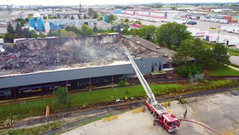 Firefighter-On-Firetruck-Ladder-Overviewing-Chemical-Factory-Building-Burnt-By-Massive-Fire