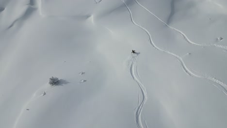 Antena-Siguiendo-A-Un-Joven-Esquiador-Deportivo-Abajo-De-La-Cordillera-Del-Glaciar-Cubierto-De-Nieve-En-Un-Paisaje-Alpino-Nevado