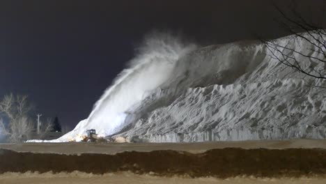 Snow-plow-firing-snow-onto-massive-mound-in-Montreal,-Canada