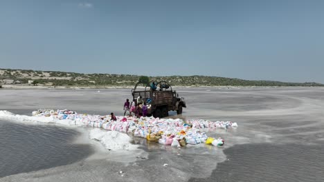 Aerial-Circle-Dolly-View-Of-Workers-Loading-Up-Bags-On-Back-On-Truck-On-Salt-Lake-In-Sindh