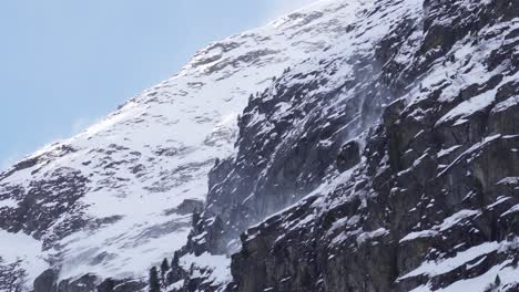 Close-up-of-snow-getting-blown-around-on-a-mountain-cliff-ridge-on-a-snowy-rocky-glacier-slope
