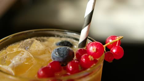 Slow-backwards-reveal-of-hurricane-cocktail-with-red-currant-and-blue-berries,-striped-paper-straw-inserted