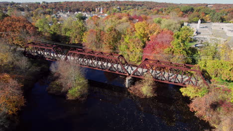 Aerial-view-of-the-trail-truss-bridge-over-the-Pawtuxet-River,-the-autumn-forests-on-the-banks