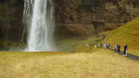 Long-line-of-tourists-on-path-and-taking-pictures-of-Seljalandsfoss-waterfall-in-Iceland