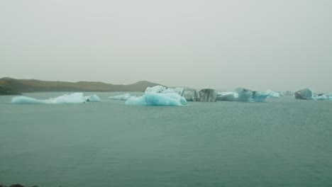 Wide-pan-of-blue-icebergs-floating-on-Lake-Jokulsarlon-on-a-cloudy-day