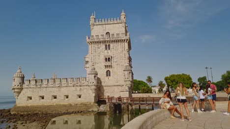 Tourists-taking-pictures-with-the-Belem-Tower-and-its-wooden-pier-in-the-background,-Lisbon,-Portugal
