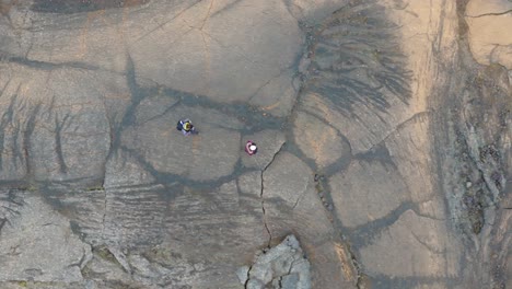 Aerial:-two-people-exploring-cracked-Icelandic-terrain-with-unique-rock-formations