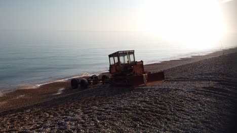 Aerial-4K-Drone-footage-of-an-old-boat-tractor-on-the-stoney-beach-of-Weybourne-Beach,-North-Norfolk