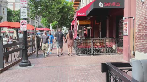 The-Gaslamp-district-walking-behind-a-couple-and-passing-cafes-and-restaurants-in-Downtown-San-Diego,-CA