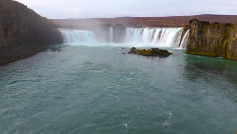 Isländischer-Wasserfall,-Der-In-Einen-Türkisfarbenen-Fluss-Mit-Schroffen-Klippen-Stürzt