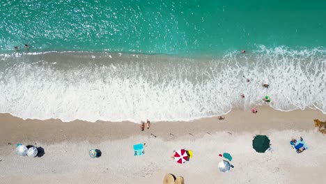 Panoramic-aerial-drone-of-beautiful-beach-with-people-playing-in-the-water-and-relaxing-on-the-shore