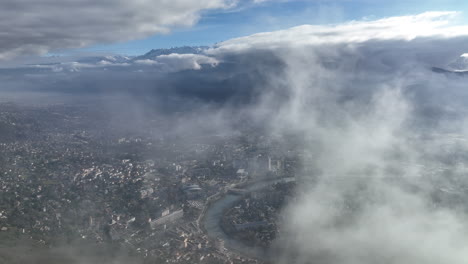 Toma-Aérea-A-Gran-Altitud-Sobre-La-Ciudad-De-Grenoble,-Francia,-Día-Soleado,-Montañas-En-La-Parte-Trasera.