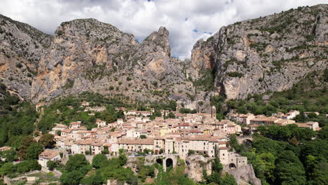 Beautiful-french-village-Moustiers-Sainte-Marie-beneath-a-mountain-France-aerial