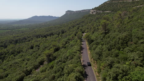 Electric-car-driving-on-a-road-passing-through-a-forest-south-of-France-sunny