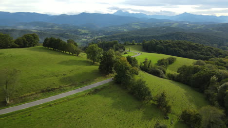 An-aerial-view-showcases-winding-roads-through-green-meadows,-framed-by-hills