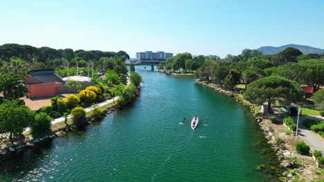 Rowing-on-the-La-Siagne-River,-aerial-view,-with-a-train-and-sea-in-the-backdrop