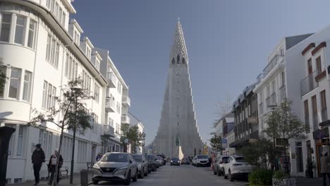 Concurrida-Calle-De-La-Ciudad-Llena-De-Coches-Y-Peatones-Caminando,-Vista-De-La-Iglesia-Hallgrimskirkja-En-Islandia