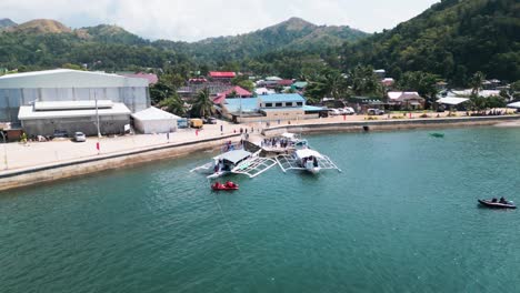 Local-fishing-boats-docked-near-pier-pull-back-aerial-view,-Philippines