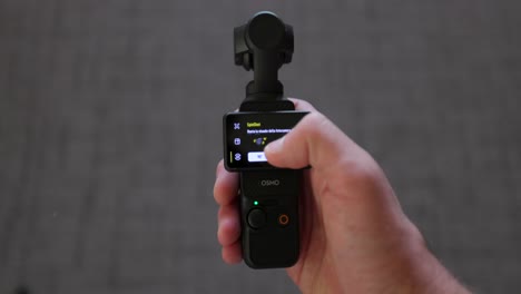 Dji-Osmo-Pocket-3-Sostenido-En-La-Mano-Y-La-Interfaz-De-Pantalla-En-Uso-Y-El-Cabezal-Del-Cardán-Girando-360