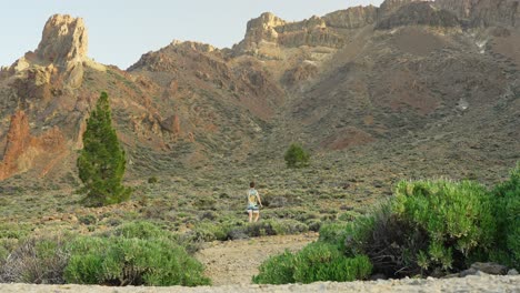 Man-walking-by-himself-towards-the-mountains-in-colored-shirt-and-shorts,-static-wide-angle