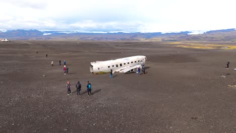 drone-aerial-view-of-the-famous-carcass-of-the-DC3-plane-crashed-in-Iceland-on-a-vast-expanse-of-black-earth-with-a-few-visitors-coming-to-admire-it