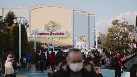 Besucher-In-Masken-In-Den-Universal-Studios-Japan-Mit-Snoopy-Studio-Und-Dem-Fliegenden-Snoopy-Im-Hintergrund