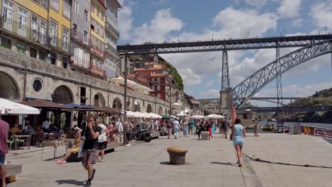 Turistas-Caminando-Por-El-Muelle-Bajo-El-Puente-Luis-I-En-Oporto,-Portugal