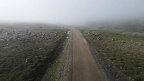 Plunge-into-mystery-with-this-drone-shot,-navigating-a-dirt-road-on-a-mountain-that-disappears-into-enveloping-mist,-the-path-ahead-obscured,-promising-unseen-wonders