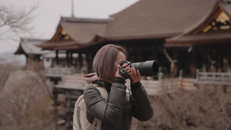 Young-Asian-woman-in-winter-clothing-taking-pictures-with-camera-in-front-of-Kiyomizudera-Temple-in-winter