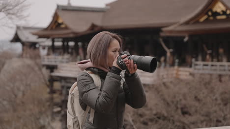 Young-Asian-woman-in-winter-clothing-taking-pictures-in-front-of-Kiyomizudera-Temple-in-Kyoto,-Japan