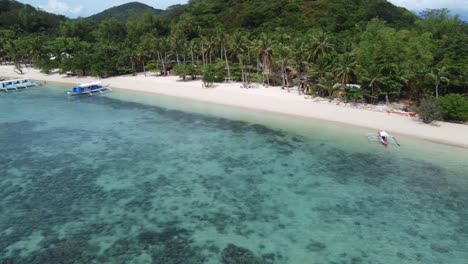People-at-Coco-Beach-resort-huts-on-Bulalacao-island-in-Coron,-Philippines-with-island-hopping-Boats-in-blue-clear-water