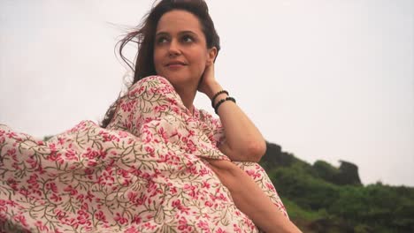 An-Indian-woman-reclines-gracefully-on-the-windswept-grass-on-a-breezy-day,-her-floral-dress-swaying-with-the-wind's-gentle-movements-in-Panaji,-Goa,-India-on-31-08-2023