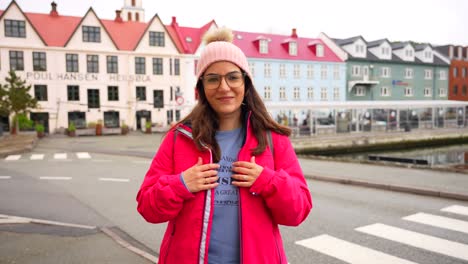 Happy-young-woman-shows-Faroe-Islands-t-shirt-with-picturesque-town-of-Torshavn-behind