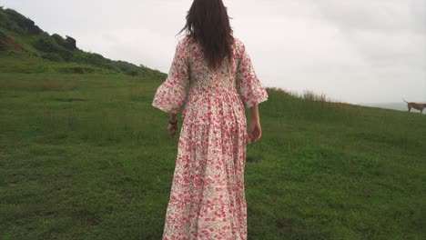 A-young-Indian-woman-enjoys-a-peaceful-stroll-with-her-dog-through-a-verdant,-grassy-forest-beside-the-sea-on-a-tranquil,-overcast-day-in-Panaji,-Goa,-India-on-31-08-2023