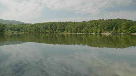 Panorama-across-scenic-lake-with-cloud-reflections-and-tree-lined-shore