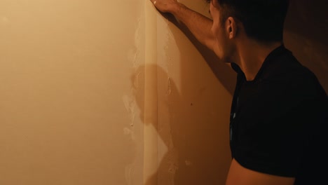 A-young-man-measures-protective-strips-on-the-wall-before-wallpapering