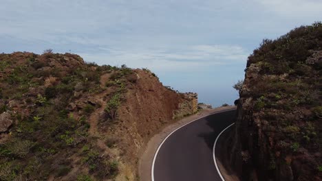 Cinematic-flying-along-road-leading-along-rocky-coastline-mountain-ranges-on-cliff-in-Tenerife