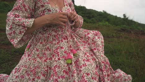 An-unidentifiable-Indian-woman,-adorned-in-a-floral-dress,-partakes-in-a-delightful-interaction-with-a-bouquet-of-flowers-in-her-hands-amidst-field-near-the-sea-in-Panaji,-Goa,-India-on-31-08-2023