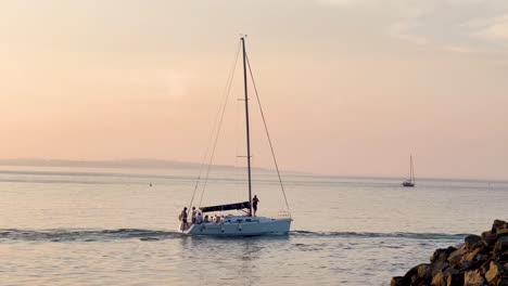 Seguimiento-Manual-De-Un-Velero-En-Las-Tranquilas-Olas-Al-Atardecer,-Howth,-Irlanda