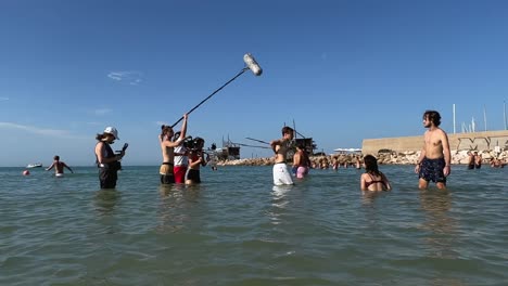 Filmtruppe-Badet-Im-Wasser-Und-Filmt-Szenen-Von-Jungen-Und-Mädchen,-Die-In-Der-Sommersaison-Im-Meer-Für-Die-Filmproduktion-Spielen