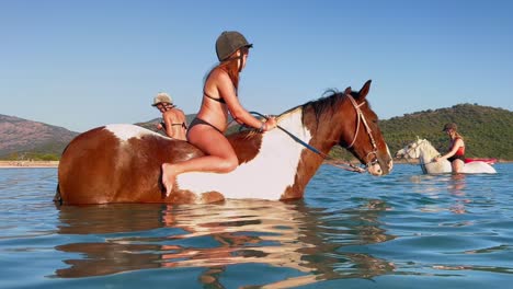 Kid-have-fun-bareback-riding-horse-in-sea-water-in-summer-season-with-other-people