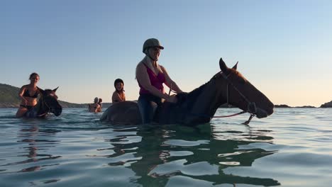 People-have-fun-bathing-and-bareback-riding-horse-in-sea-water-in-summer-season-at-sunset