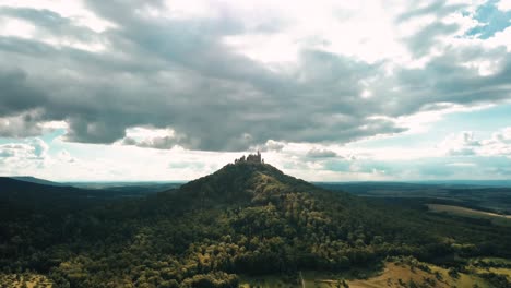 Drone-view-tilting-down-of-the-Hohenzollern-Castle-surrounded-by-a-forest-atop-Hohenzollern-Mountain-and-the-beautiful-countryside-in-Zollernalbkreis,-Germany