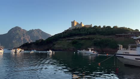 Tour-boat-at-Girolata-village-of-Scandola-peninsula-nature-reserve-at-sunset-in-summer-season,-Corsica-island-in-France