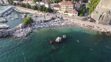 Aerial-Herceg-Novi-Beach,-Montenegro-with-bustling-marina-and-swimmers