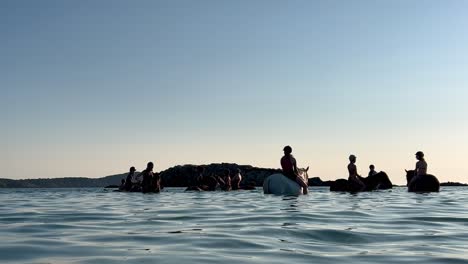 Gente-Bañándose-Y-Montando-A-Caballo-Sumergido-En-Agua-De-Mar-En-La-Temporada-De-Verano-Al-Atardecer