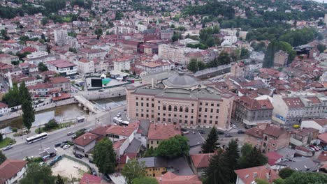 Aerial:-Sarajevo-showcasing-iconic-City-Hall-beside-the-winding-river